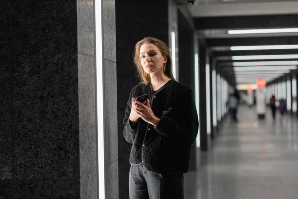 Hübsche junge Frau in schwarzer Jacke posiert in modernem Gebäude mit Leuchtstoffröhren in Berlin — Stockfoto