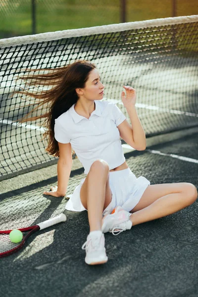 Жіночий тенісист сидить навпроти вітру, молода жінка з довгим волоссям сидить у білому одязі біля ракетки з м'ячем і тенісною сіткою, розмитим фоном, Маямі, знакове місто, тенісний корт, понаднормова — стокове фото