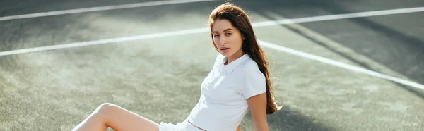 Tennisspielerin ruht sich nach dem Spiel aus, junge Frau sitzt in weißem Outfit auf Asphalt und blickt in die Kamera, verschwommener Hintergrund, Miami, Tennisplatz, Ausfallzeit, Poloshirt, Banner — Stockfoto