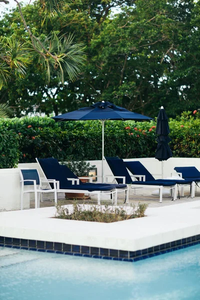 Complejo de lujo, vacaciones y concepto de vacaciones, tumbonas y sillas al aire libre cerca de sombrillas azules alrededor de palmeras verdes y plantas tropicales junto a la piscina al aire libre en el hotel, verano - foto de stock