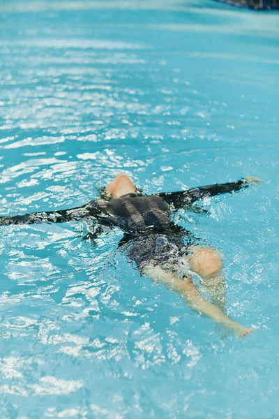 Femme insouciante en vêtements noirs nageant dans l'eau bleue de la piscine extérieure dans un complexe de luxe à Miami, liberté, eau chatoyante, bonheur, liberté, détente, station balnéaire à Miami — Photo de stock