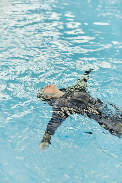 Femme insouciante en vêtements noirs nageant dans l'eau bleue de la piscine publique dans un complexe de luxe à Miami, eau chatoyante, liberté, escapade estivale, détente, station balnéaire à Miami — Photo de stock