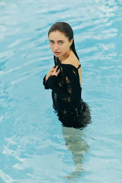 Senza trucco, bella e sexy donna bruna in maglia nera in posa all'interno della piscina all'aperto durante le vacanze a Miami, seducente, resort di lusso, Florida — Foto stock