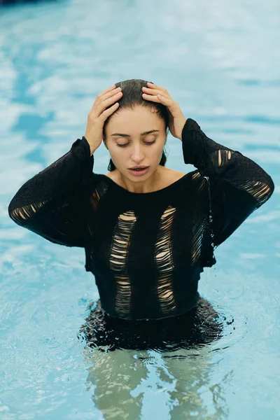 Senza trucco look, bella e sexy donna in abito nero a maglia posa all'interno della piscina all'aperto durante le vacanze a Miami, seducente, resort di lusso, bellezza naturale — Foto stock
