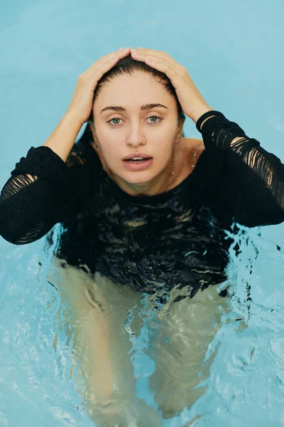 Senza trucco, bella e sexy donna bruna in maglia nera in posa all'interno della piscina all'aperto durante le vacanze a Miami, bellezza naturale, resort di lusso, Florida, vista dall'alto — Foto stock
