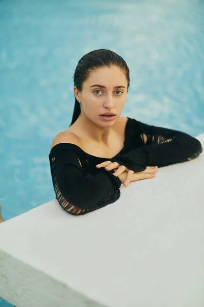 Resort de lujo en Miami, hermosa mujer con piel bronceada en traje de baño negro nadando en la piscina pública, posando y disfrutando de sus vacaciones de verano, sin maquillaje - foto de stock