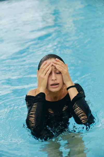 Resort de lujo en Miami, hermosa mujer con piel bronceada tocando su cara mojada después de nadar en la piscina pública, posando y disfrutando de sus vacaciones de verano, sin maquillaje - foto de stock