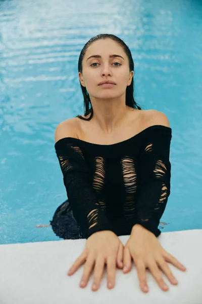 Luxusresort in Miami, sexy Frau mit gebräunter Haut, die in die Kamera schaut, im öffentlichen Schwimmbad, posiert und genießt ihren Sommerurlaub, kein Make-up-Look, lebhafte Atmosphäre — Stockfoto