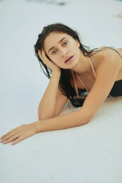 Brünette Frau im schwarzen Bikini, sexy Model mit nassen Haaren posiert im Luxusresort in Miami, Florida, USA, blickt in die Kamera, verschwommener Hintergrund, legt sich auf weiße Oberfläche, Entspannung am Pool — Stockfoto