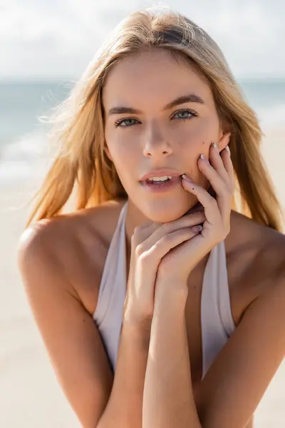 Eine junge blonde Frau posiert am Miami Beach, die Hände vor dem Gesicht, tief in Gedanken und Kontemplation. — Stockfoto