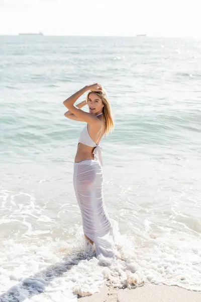 Eine junge blonde Frau steht selbstbewusst an einem Strand in Miami und blickt an einem sonnigen Tag auf die riesigen Wellen des Ozeans. — Stockfoto