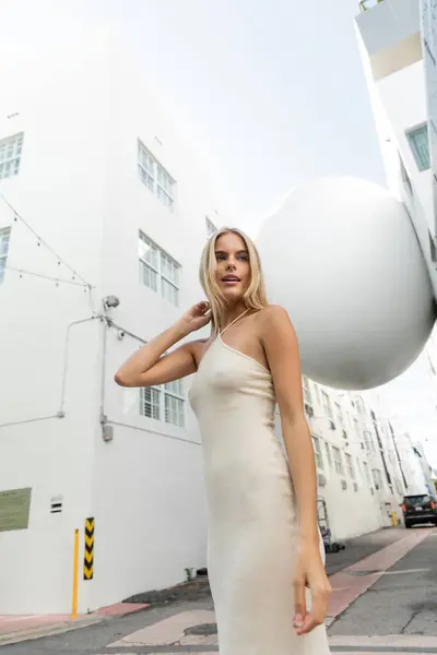 Una splendida donna bionda in un abito bianco fluente colpisce una posa per una foto in un ambiente vibrante di Miami. — Foto stock