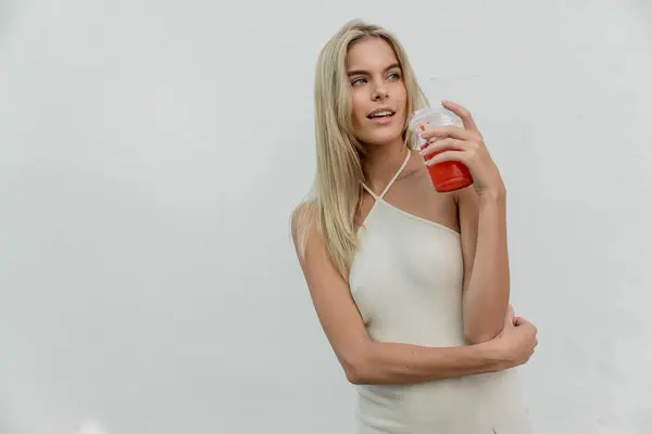Une jeune, belle femme blonde à Miami tenant une tasse rouge tout en portant une robe blanche fluide sous le soleil chaud. — Photo de stock