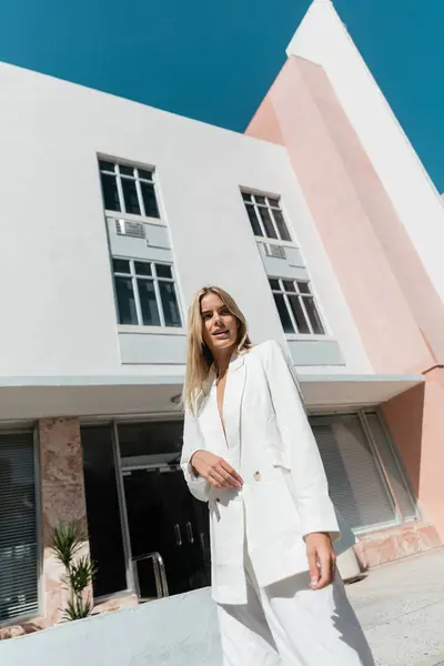 A young blonde woman stands gracefully in front of a striking pink and white building in Miami. — Stock Photo