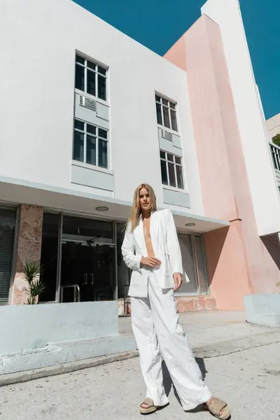 Une jeune femme blonde se tient gracieusement devant un bâtiment rose et blanc à Miami. — Photo de stock