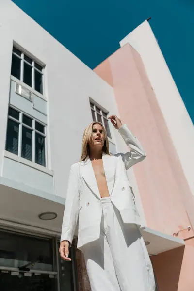 A young, beautiful blonde woman standing gracefully in front of a vibrant pink and white building in Miami. — Stock Photo