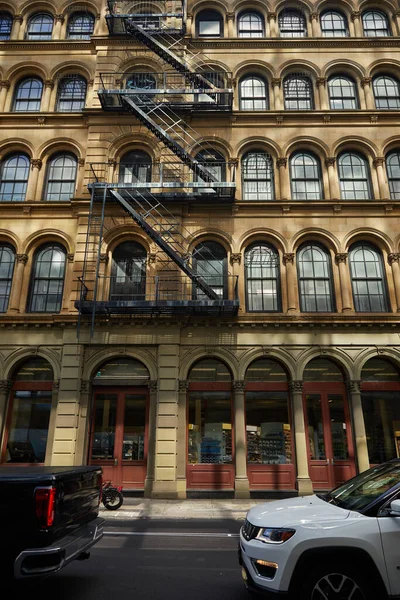 Coches que se mueven en la carretera a lo largo del edificio vintage con escaleras de escape de incendios en la ciudad de Nueva York, vista a la calle - foto de stock