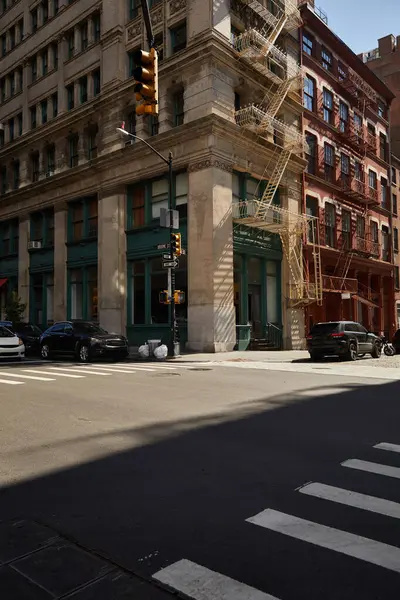 Edificio de esquina con escaleras de escape de incendios y coches en cruce en la calle del centro de la ciudad de Nueva York - foto de stock