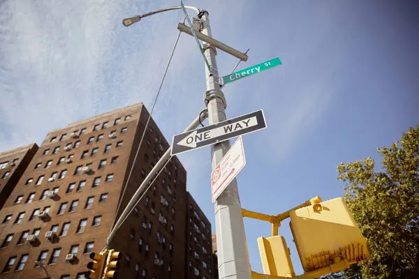 Низький кут зору вуличного полюса з дорожніми знаками, що показують напрямок біля будівлі з червоної цегли в Нью-Йорку — стокове фото