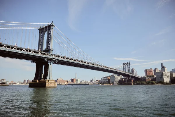 Живописный вид на Манхэттенский мост под голубым небом над восточной рекой с городским пейзажем Нью-Йорка — стоковое фото