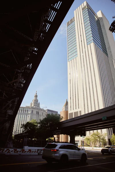 Vue panoramique du gratte-ciel près de la voiture se déplaçant sur la chaussée sous le pont dans la ville de New York, atmosphère urbaine — Photo de stock