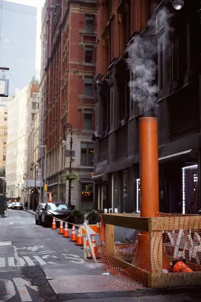 Tubo de ventilación humeante en la calzada estrecha en la ciudad de Nueva York, paisaje urbano metrópolis - foto de stock