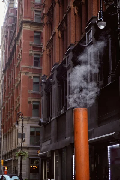 Tubo de ventilación humeante cerca de edificios de piedra en el centro de distrito de la ciudad de Nueva York, escena de la calle - foto de stock