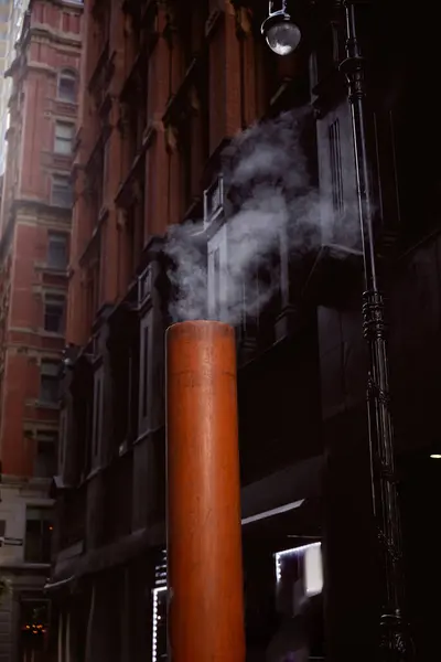 Fumante tubo di ventilazione sulla strada vicino a edifici in pietra su sfondo sfocato nella città di New York — Foto stock