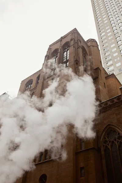 Low angle view of red brick catholic church near steam on street in new york city, urban atmosphere — Stock Photo