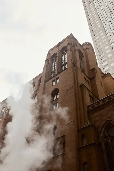 Blick auf die katholische Kirche aus rotem Backstein in der Nähe von Dampf und Wolkenkratzer auf der Straße in New York City — Stockfoto
