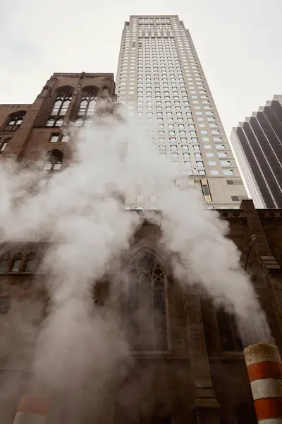 Église catholique en brique rouge et gratte-ciel près de la vapeur sur la rue dans la ville de New York, vue à angle bas — Photo de stock