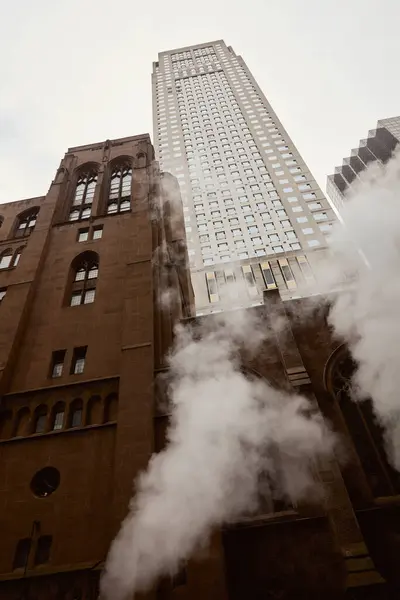 Low angle view of red brick catholic church near modern skyscraper and steam on new york city street — Stock Photo