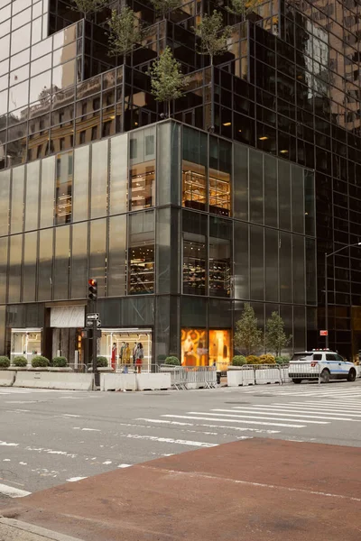 Edificio moderno con fachada de vidrio y tienda de ropa en cruce en avenida en la ciudad de Nueva York - foto de stock