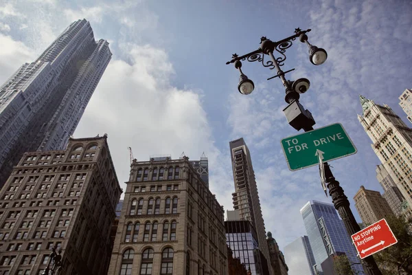 Poste de calle con linternas y señales de tráfico contra rascacielos en la ciudad de Nueva York, vista de ángulo bajo - foto de stock