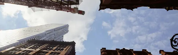 Vista inferior de edificios modernos y antiguos contra el cielo azul nublado en la ciudad de Nueva York, bandera - foto de stock
