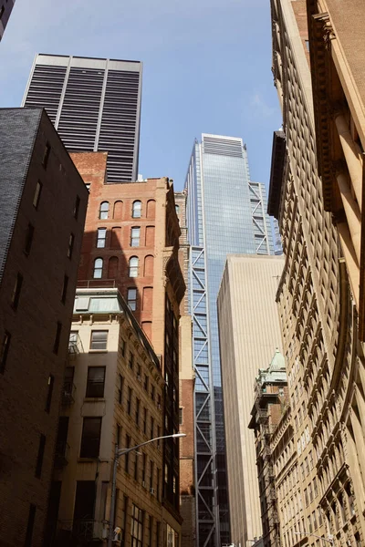 Vista de ángulo bajo de rascacielos modernos y edificios antiguos contra el cielo azul en la ciudad de Nueva York - foto de stock