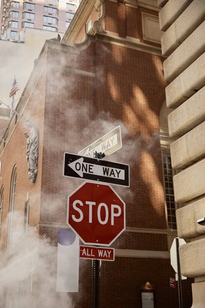 Señales de tráfico cerca de vapor y edificios antiguos en la calle de la ciudad de Nueva York, entorno urbano escena - foto de stock