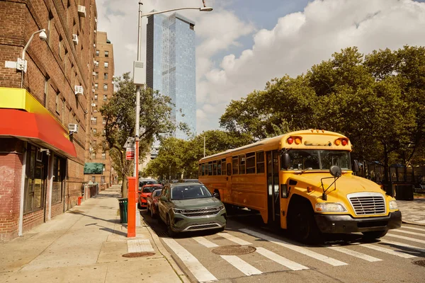 Autobús escolar amarillo y coches en el paso de peatones cerca de árboles con follaje de otoño en la ciudad de Nueva York, escena de otoño - foto de stock