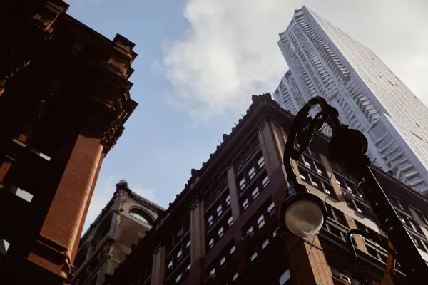 Низкий угол обзора фонаря возле современных и старинных зданий против голубого облачного неба в Нью-Йорке — стоковое фото
