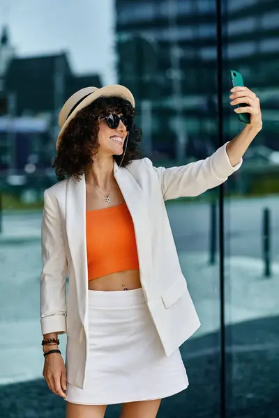 Eine Frau in weißem Blazer und orangefarbenem Oberteil macht ein Selfie, während sie die Stadt erkundet. — Stockfoto