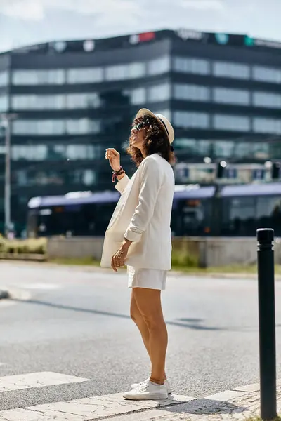 Eine Frau im weißen Outfit steht auf einem Fußgängerüberweg in einer europäischen Stadt. — Stockfoto
