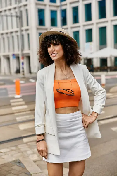 Eine elegante Frau in weißem Blazer, orangefarbenem Top und weißem Rock geht eine europäische Straße entlang. — Stockfoto