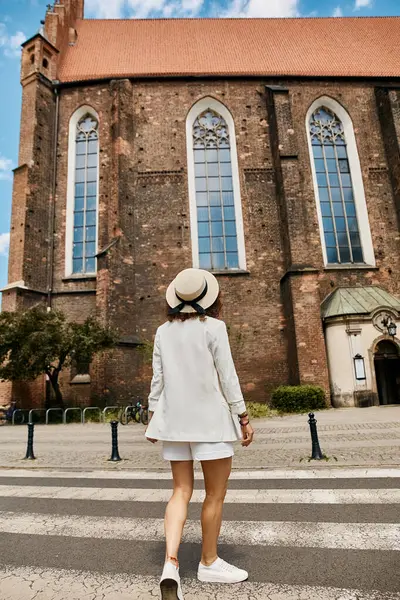 Una donna elegante cammina davanti a una chiesa storica durante il suo viaggio europeo. — Foto stock