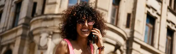 Eine Frau mit Sonnenbrille und rosa Oberteil lächelt bei einem Anruf während einer Europareise. — Stockfoto