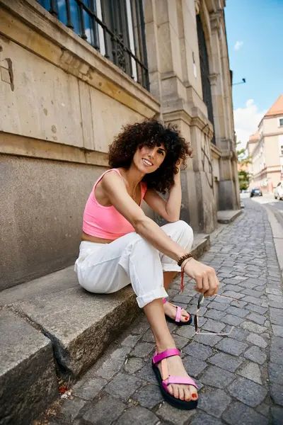 Eine Frau in schicker Kleidung sitzt auf einer Kopfsteinpflasterstraße in Europa und genießt die Sommersonne. — Stockfoto