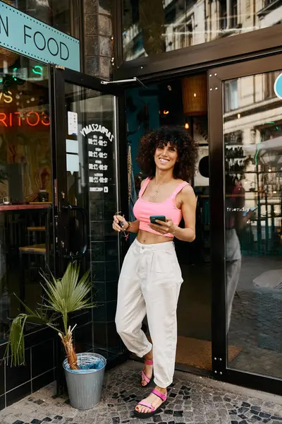 Uma mulher na moda de calças brancas e rosa sorri quando sai de um café europeu. — Fotografia de Stock