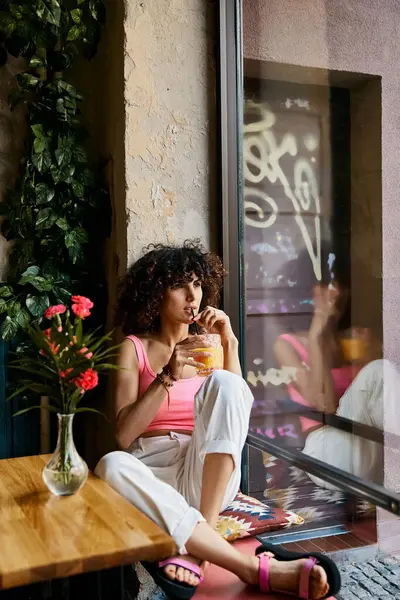 A woman in stylish attire enjoys a drink while sitting by a window in a European cafe. — Stock Photo