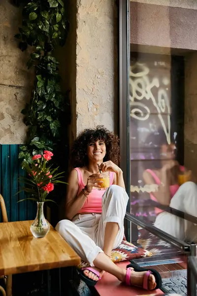 Женщина в розовом наслаждается напитком сидя у окна в европейском кафе. — стоковое фото