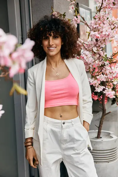 A stylish woman in a pink crop top and white blazer enjoys the springtime weather while strolling through a European city. — Stock Photo