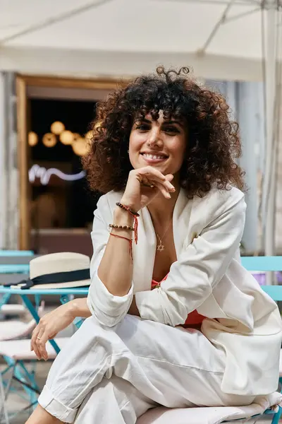 Uma mulher em um blazer branco senta-se em uma cadeira, olhando elegante e relaxado enquanto desfruta de sua viagem europeia. — Fotografia de Stock